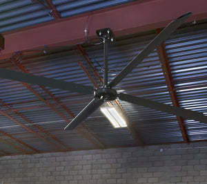 ECO HVLS Industrial ceiling fan mounted in a warehouse setting with metal beams and brick wall.